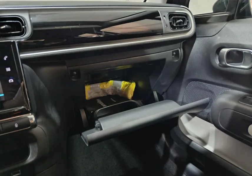 Intérieur de la Citroën C3 2024 gris foncé, vue côté passager avec boîte à gants ouverte et tableau de bord noir brillant.