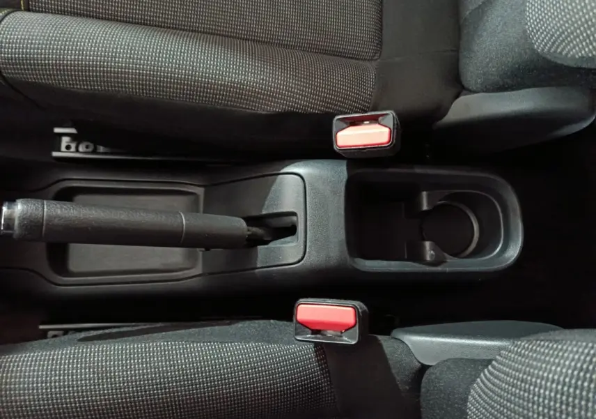 Vue plongeante sur la console centrale noire de la Citroën C3 2024, avec frein à main manuel et ceintures rouges.