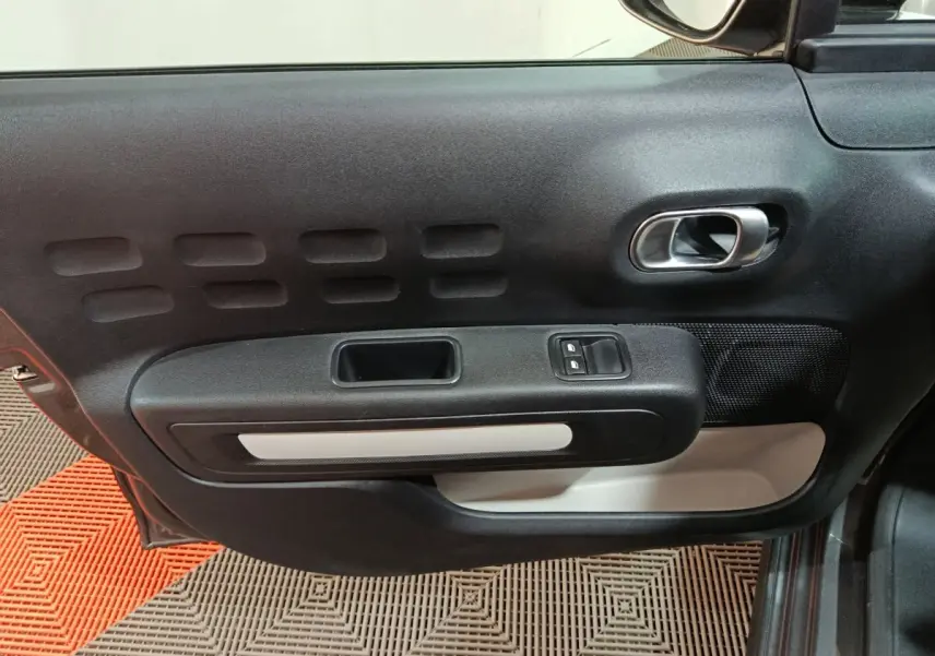 Vue intérieure de la porte côté conducteur d'une Citroën C3 gris foncé, avec commandes de vitres et poignée argentée.