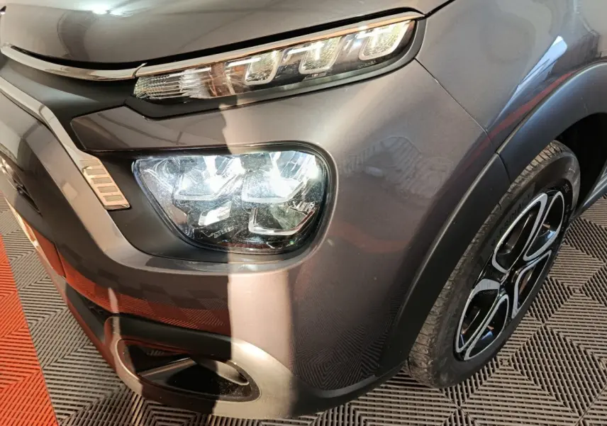 Gros plan sur l'avant droit gris foncé du Citroën C3 2024, mettant en valeur le phare LED et la jante noire à motifs.