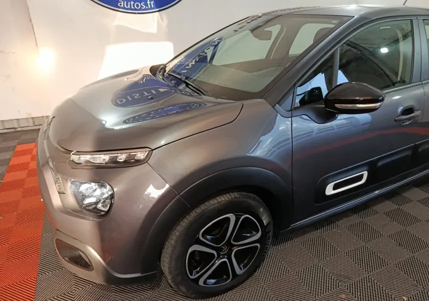 Vue 3/4 avant droit d'une Citroën C3 gris foncé avec phares LED et protections latérales noires à insert blanc.