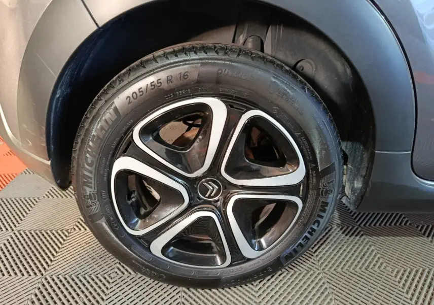 Gros plan sur la roue avant gauche d'une Citroën C3 gris foncé, avec jante noire et inserts argentés distinctifs.