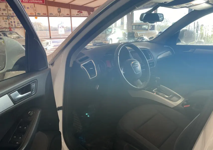 Intérieur de l'Audi Q5 blanc 2012 vu côté conducteur, montrant le volant, tableau de bord et console centrale.