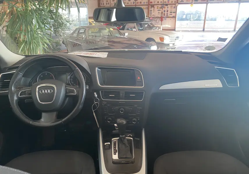 Vue intérieure avant de l'Audi Q5 blanc 2012, tableau de bord avec volant multifonction et console centrale automatique.