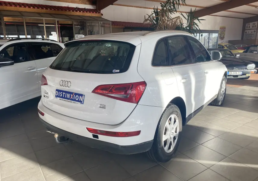 Audi Q5 blanc vue 3/4 arrière droit en intérieur, avec attelage et feux arrière rouges distinctifs.