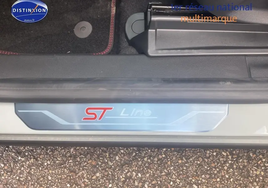 Gros plan sur la plaque de seuil ST Line du Ford Puma gris cactus, avec tapis noir et surpiqûres rouges visible.