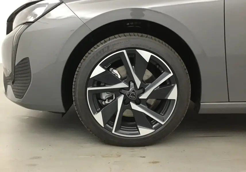 Gros plan sur la roue avant gauche d'une Peugeot 308 gris Sellenium, mettant en valeur la jante alliage au design moderne.