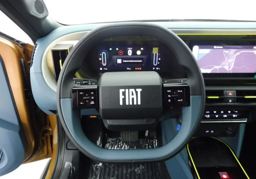 Vue rapprochée du volant noir et bleu avec logo FIAT, tableau de bord digital et intérieur bronze Luna de la Grande Panda 2025.