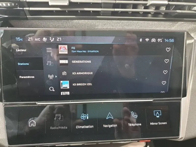 Écran tactile central de la Peugeot 308 2024 affichant les stations radio avec commandes multimédia et climatisation.