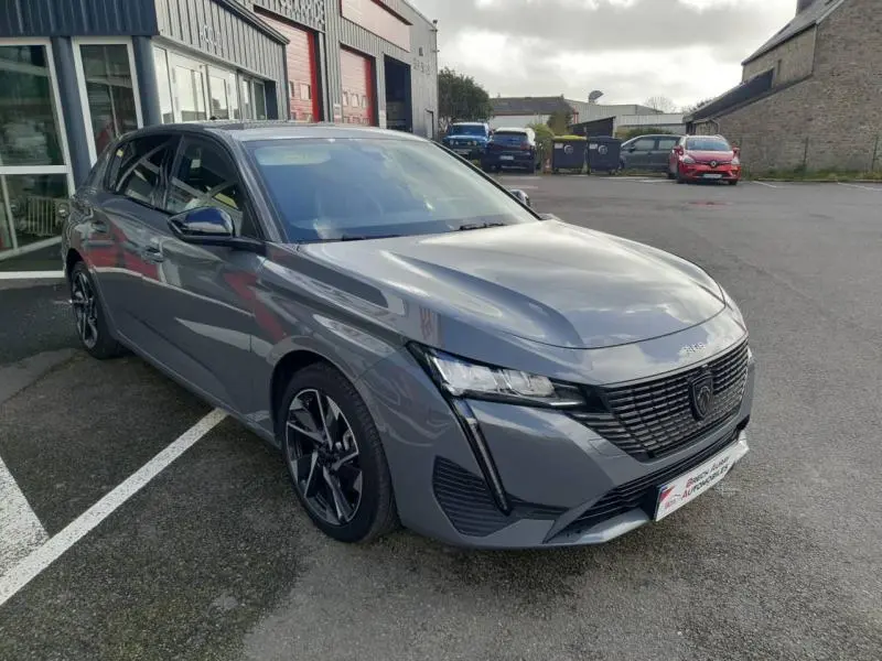 Peugeot 308 gris Sélénium vue 3/4 avant droit, avec calandre noire et phares LED distinctifs.