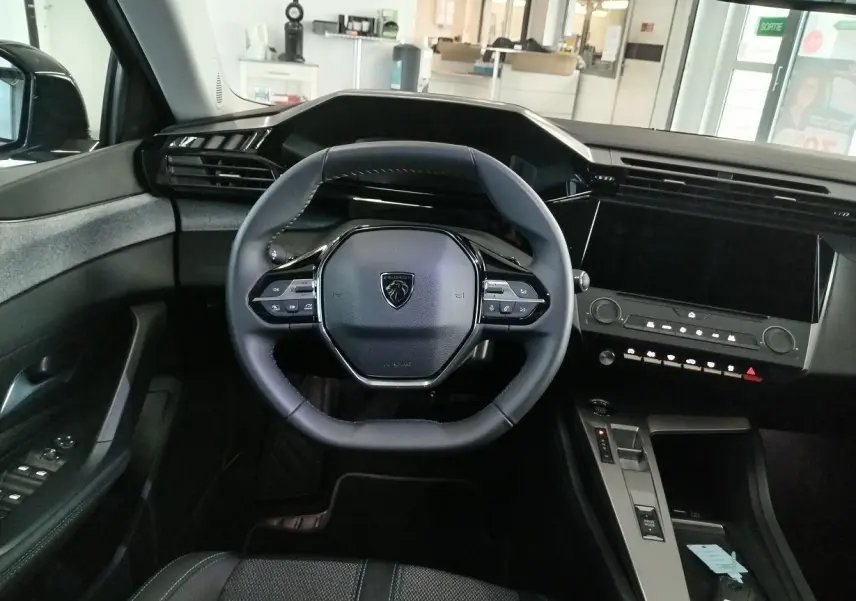 Vue intérieure frontale du poste de conduite de la Peugeot 308 SW Hybrid 145, avec volant compact et écran tactile noir.