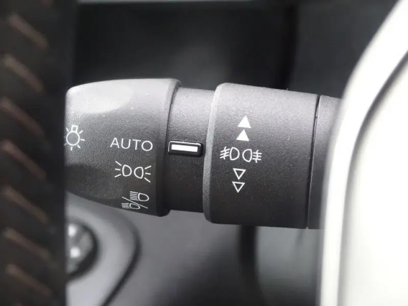 Gros plan sur la commande des feux du Peugeot Rifter gris Artense, montrant les réglages automatiques et antibrouillard.