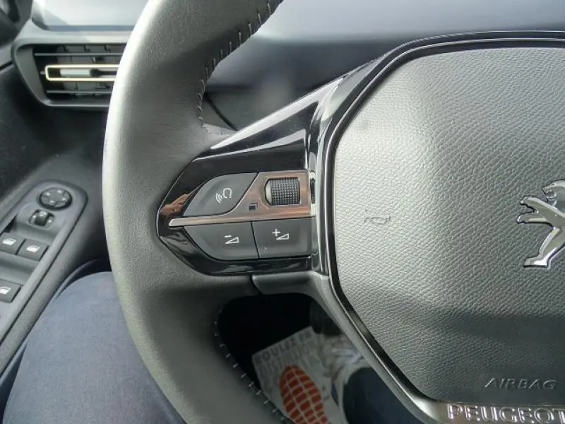 Gros plan sur le volant noir du Peugeot Rifter gris Artense, montrant les commandes audio à gauche et le logo lion central.