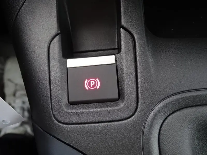 Gros plan sur le bouton de frein à main électronique illuminé en rouge dans l'habitacle noir du Peugeot Rifter gris Artense 2019.