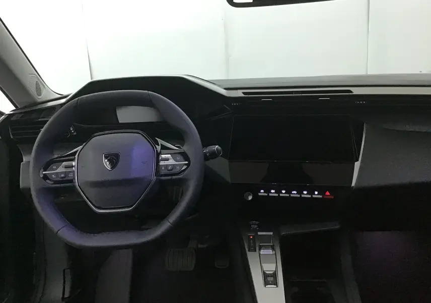 Vue intérieure du poste de conduite de la Peugeot 308 2025, volant compact et tableau de bord moderne noir.