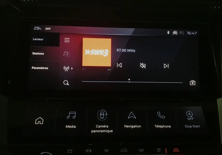 Écran tactile central de la Peugeot 308 blanc Okenite, affichant la radio FM et les options multimédia en intérieur.