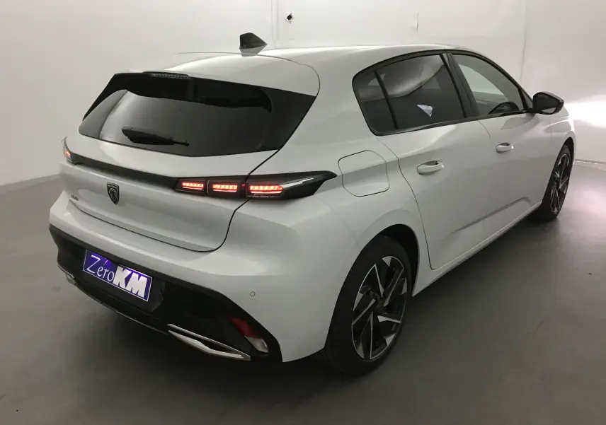 Vue 3/4 arrière droite d'une Peugeot 308 blanche Okenite avec feux arrière LED allumés et jantes alliage noires.