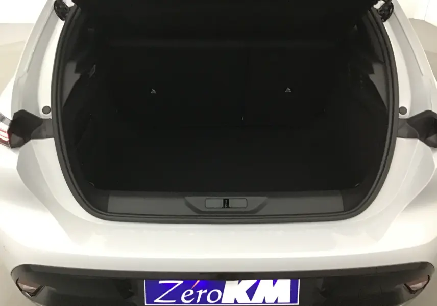Coffre ouvert vu de l'arrière d'une Peugeot 308 blanche Okenite, version 2025 avec plaque Zéro KM visible.
