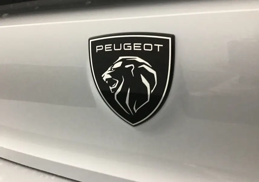 Gros plan sur l'emblème noir et blanc du lion Peugeot sur la carrosserie blanche Okenite du 308 2025.