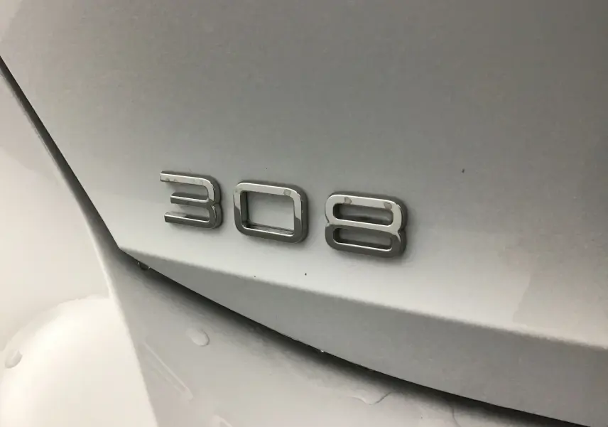 Gros plan sur l'emblème "308" en chrome sur la carrosserie blanche Okenite d'une Peugeot 308 2025.