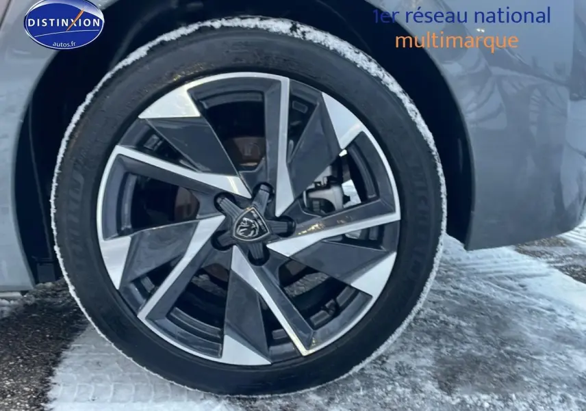 Gros plan sur la jante alu avant droite d’une Peugeot 308 gris sélénite avec neige au sol.
