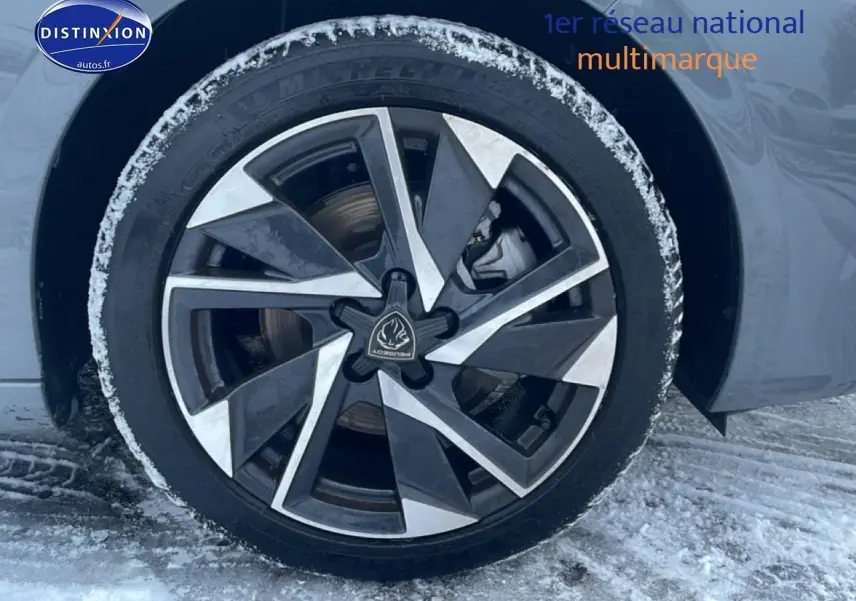 Gros plan sur la jante alu noire et argentée d'une Peugeot 308 gris sélénite, avec traces de neige autour du pneu.