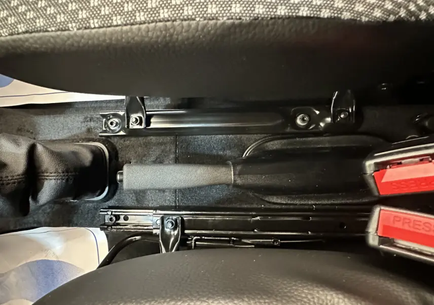 Gros plan intérieur sur le frein à main et les ceintures de sécurité rouges entre les sièges d'une Aixam Ambition E City Pack blanche.