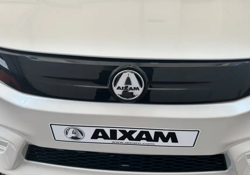 Gros plan frontal sur la calandre noire et le logo AIXAM d'une voiture électrique blanche Aixam Ambition E City Pack 2026.