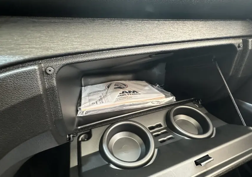 Intérieur de la boîte à gants ouverte de l'AIXAM AMBITION E CITY PACK blanc, avec porte-gobelets et manuel visible.