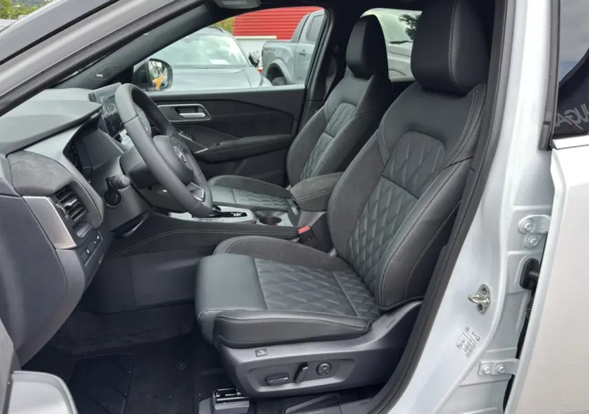 Vue intérieure côté conducteur du Nissan Qashqai blanc lunaire, sièges cuir noirs avec surpiqûres et console centrale visible.