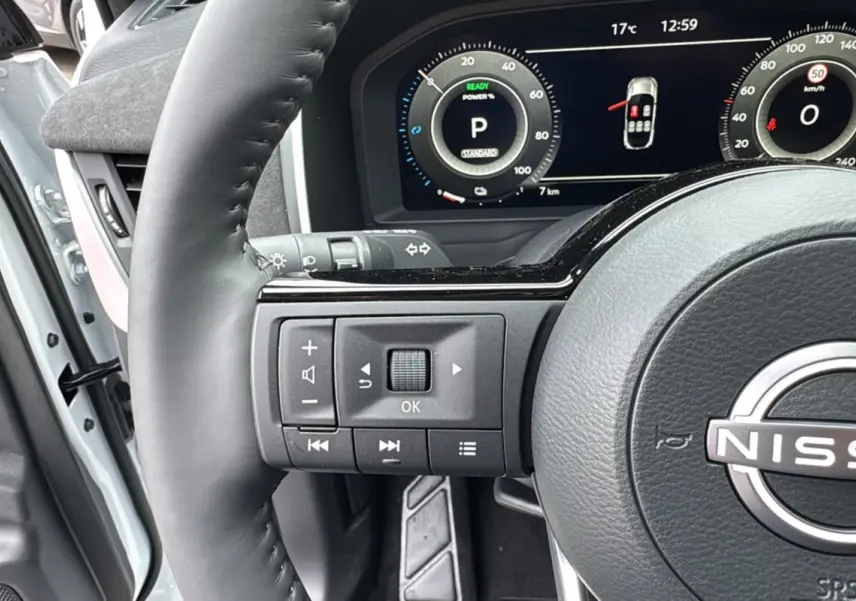 Gros plan sur le volant cuir multifonctions du Nissan Qashqai E-POWER 205 Tekna Plus, avec tableau de bord numérique allumé.