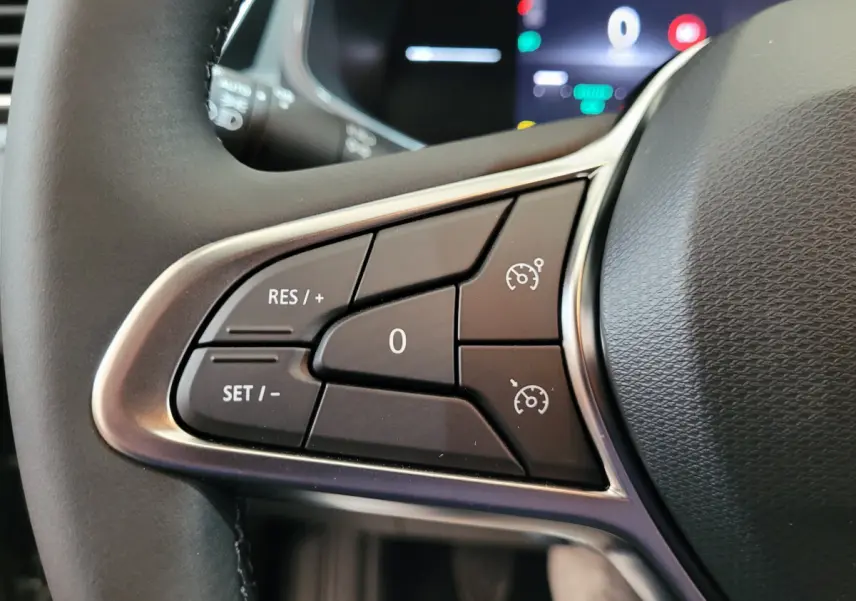 Gros plan sur les commandes du régulateur de vitesse au volant cuir d'une Renault Clio gris foncé, affichage numérique en arrière-plan.