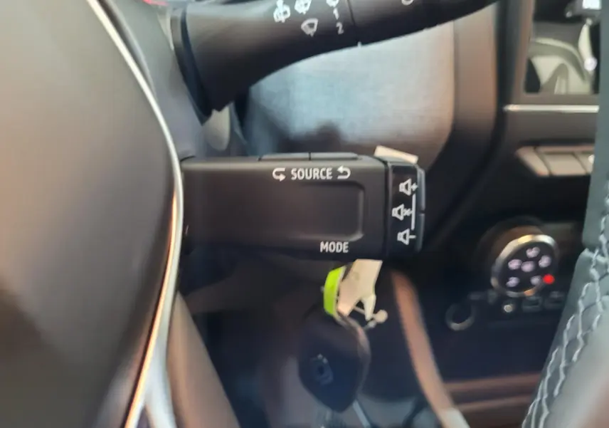 Gros plan sur la commande multifonction au volant d’une Renault Clio gris foncé, intérieur avec détails du tableau de bord.