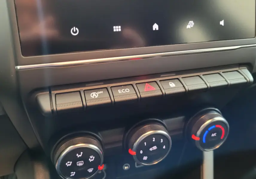 Gros plan sur la console centrale de la Renault Clio gris foncé, montrant les commandes de climatisation et les boutons multifonctions.