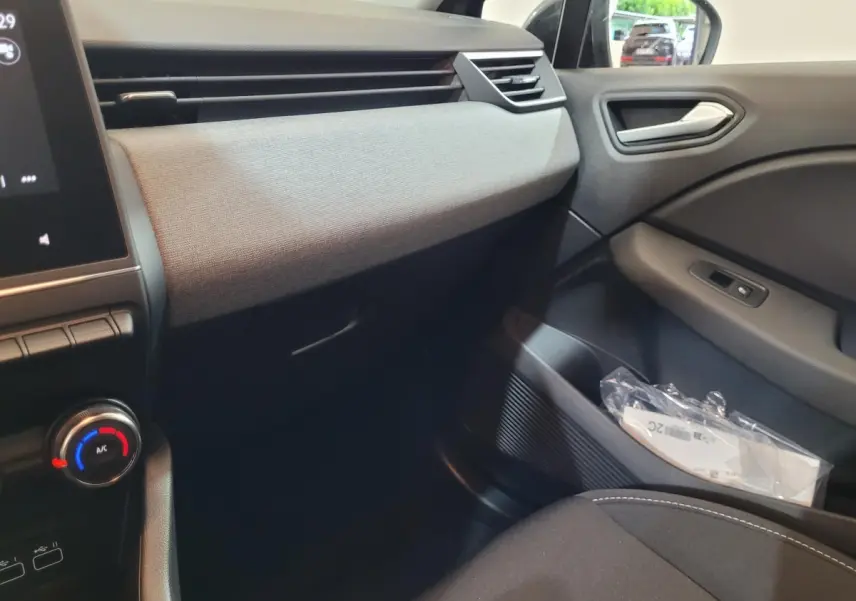 Vue intérieure côté passager de la Renault Clio gris foncé 2025, avec tableau de bord textile et commandes climatisation.