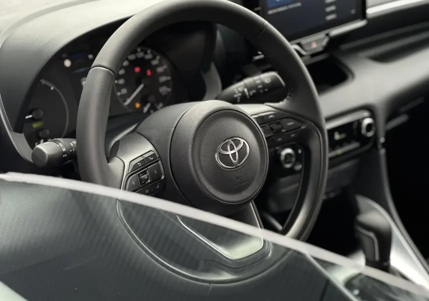 Vue rapprochée du volant en cuir noir de la Toyota Yaris 2025, avec commandes multifonctions et tableau de bord visible.