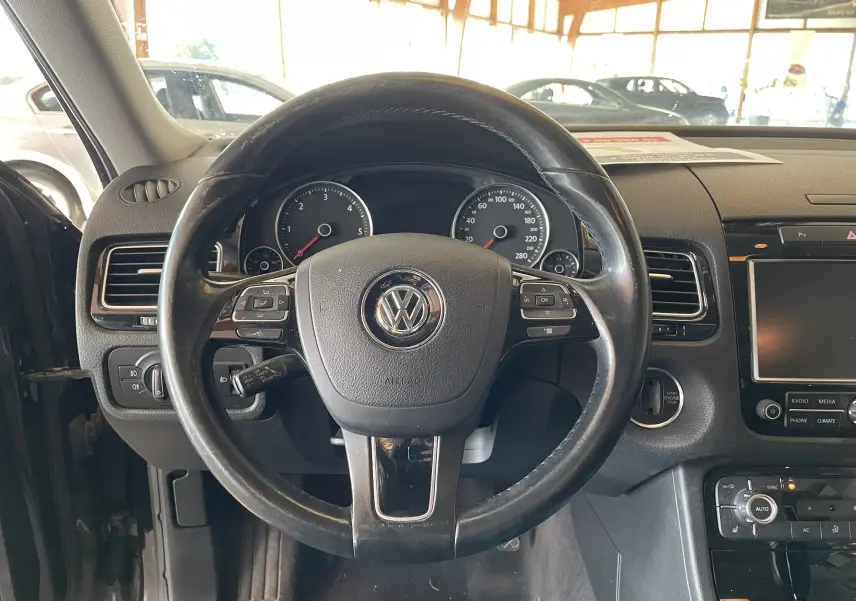 Vue rapprochée du volant en cuir noir d'un Volkswagen Touareg 2012, tableau de bord et commandes visibles.