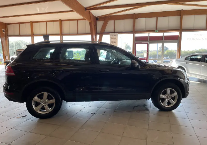 Profil côté gauche d'un Volkswagen Touareg noir 2012 en showroom, soulignant ses lignes robustes et jantes alliage.