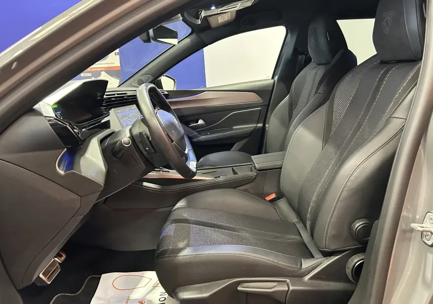 Intérieur avant droit du Peugeot 308 SW 2024 gris Sellenium, sièges cuir noirs avec logo Peugeot brodé sur appuie-tête.