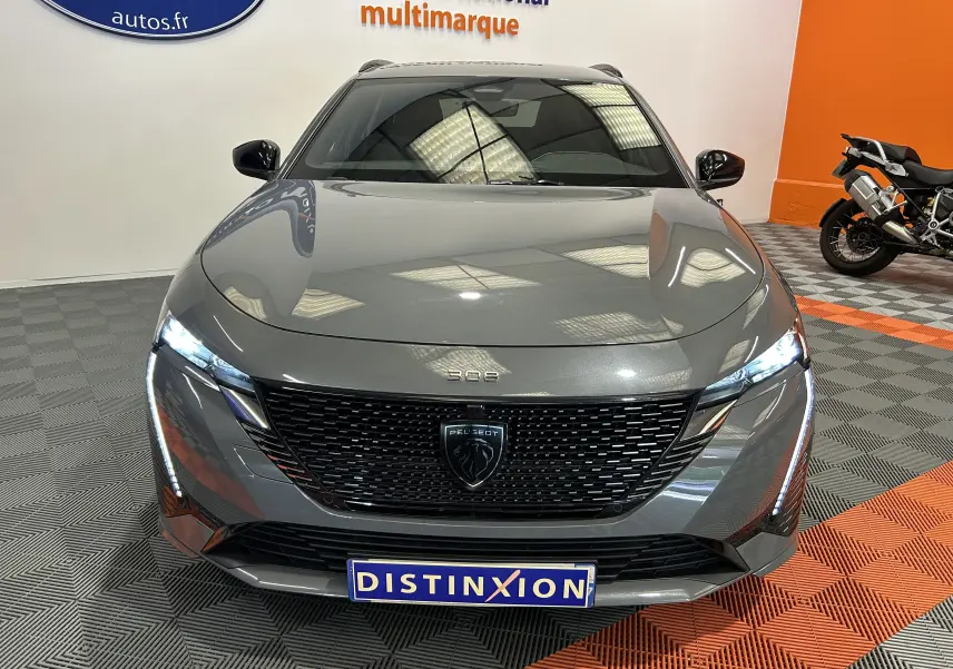 Vue avant d'une Peugeot 308 SW III GT Gris Sellenium avec calandre noire et phares LED allumés en intérieur showroom.