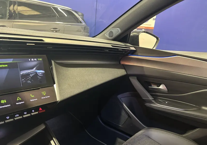 Vue intérieure côté passager de la Peugeot 308 SW 2024 gris Sellenium avec tableau de bord moderne et éclairage d'ambiance bleu.