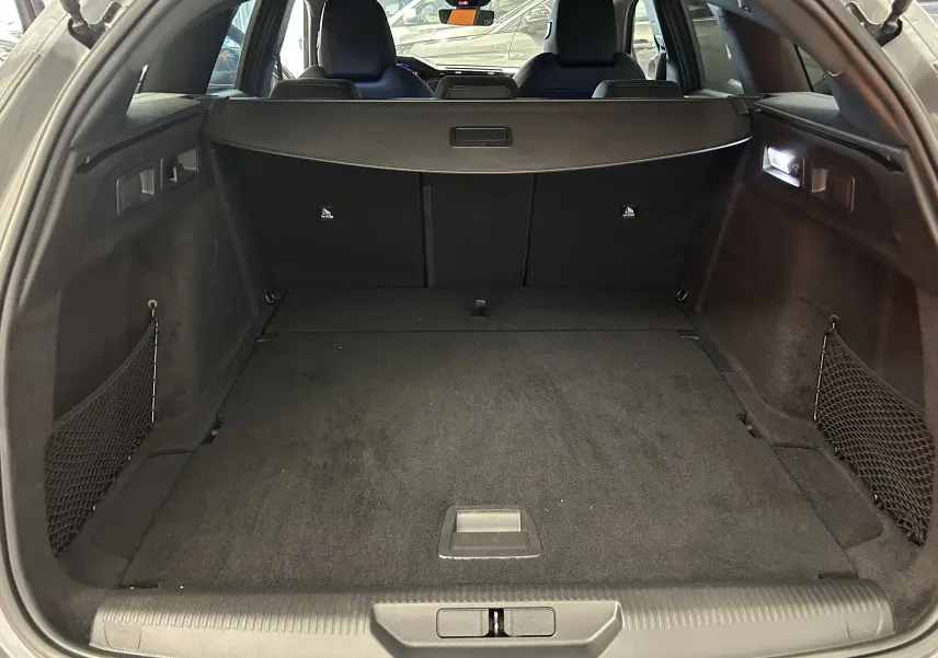 Coffre spacieux de Peugeot 308 SW III GT BlueHDi 130 gris Sellenium vu de l'arrière avec filet de rangement et éclairage intérieur.