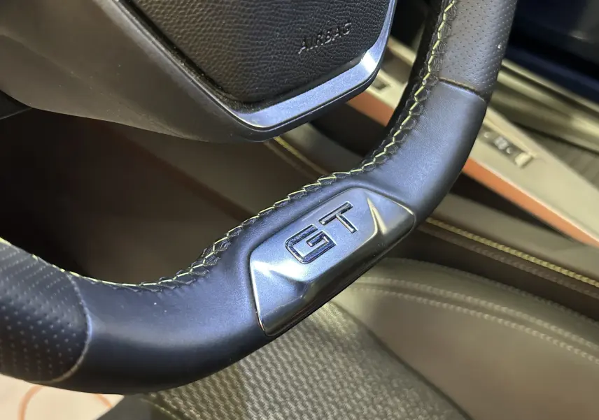 Gros plan sur le volant cuir perforé avec logo GT de la Peugeot 308 SW III GT, intérieur beige et surpiqûres contrastées.