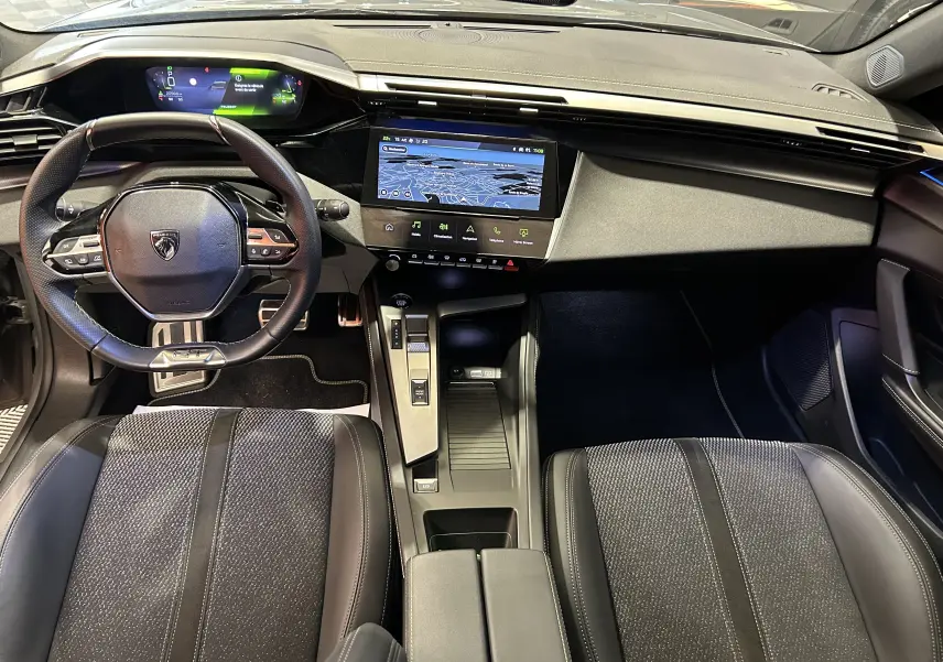 Vue intérieure de la Peugeot 308 SW III GT, tableau de bord moderne avec écran GPS et volant multifonction noir.