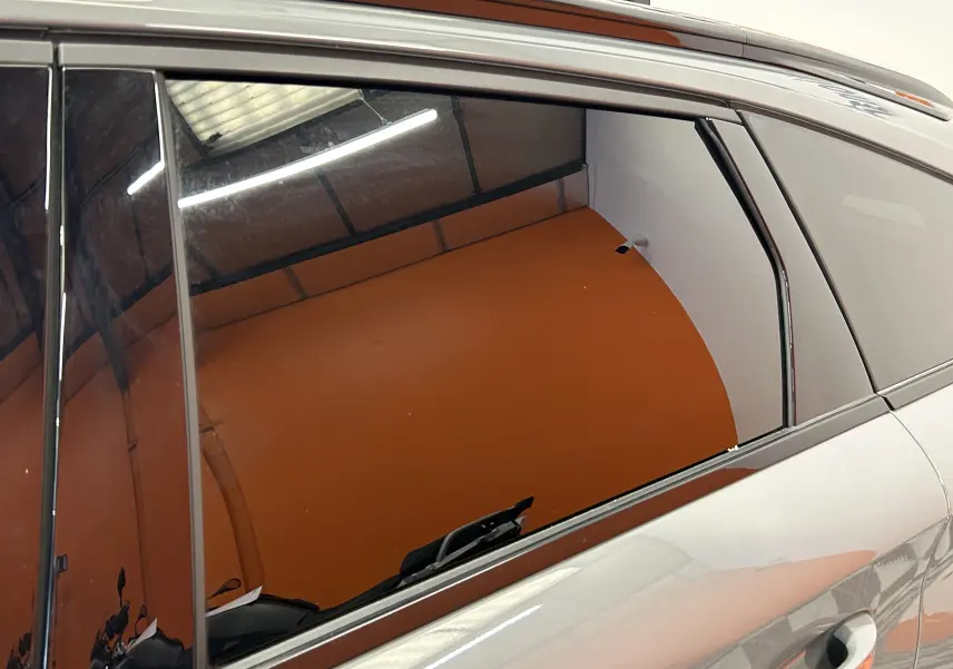 Reflet sur la vitre arrière côté gauche d'une Peugeot 308 SW gris Sellenium, montrant l'intérieur et l'environnement orange.