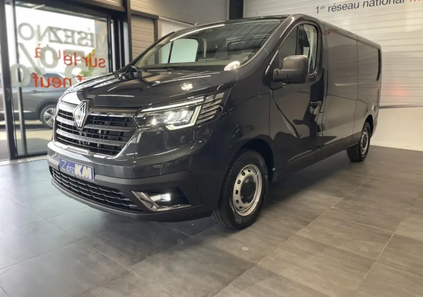 Vue 3/4 avant droit d'un Renault Trafic Fourgon gris comète avec projecteurs LED et jantes tôles 16 pouces en showroom.