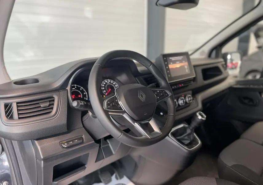 Vue intérieure du poste de conduite du Renault Trafic Fourgon gris Comète, avec volant multifonction et écran tactile central.