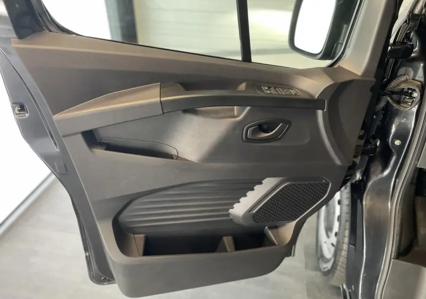 Porte côté conducteur ouverte du Renault Trafic Fourgon gris Comète, montrant les commandes de vitres et le haut-parleur intégré.