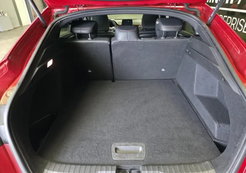 Coffre ouvert vu de l'arrière d'un Renault Arkana rouge, banquette arrière avec surpiqûres rouges visible.