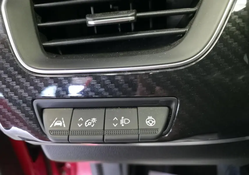 Gros plan sur les commandes d'assistance et réglages lumineux sur la planche de bord en carbone brillant du Renault Arkana Rouge Flamme.